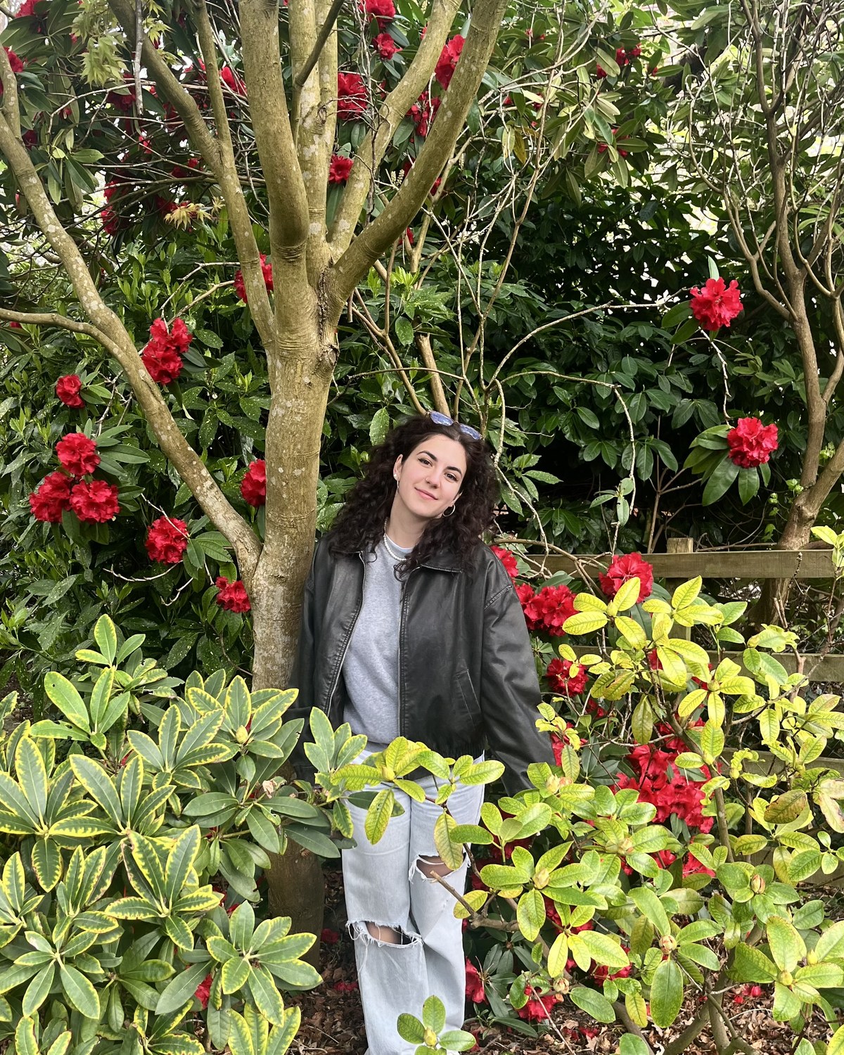 Dina, the photographer behind Afterglow, standing among red rhododendrons in bloom.